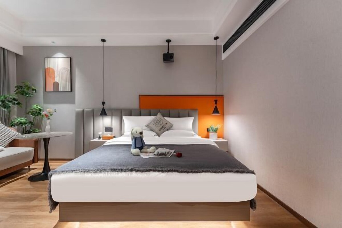 A modern bedroom with a bed, bedside tables, a nightstand, a lamp, and a wall-mounted projector.