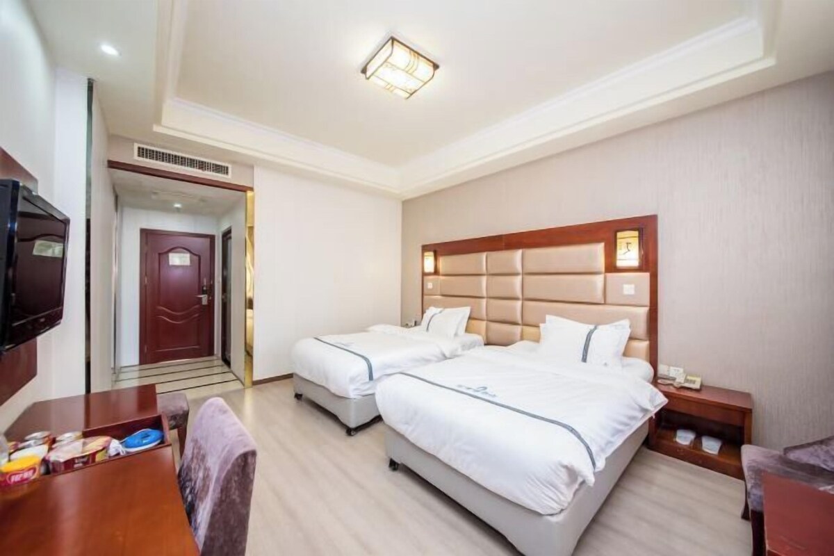 A hotel room with two beds, a desk, and a TV.