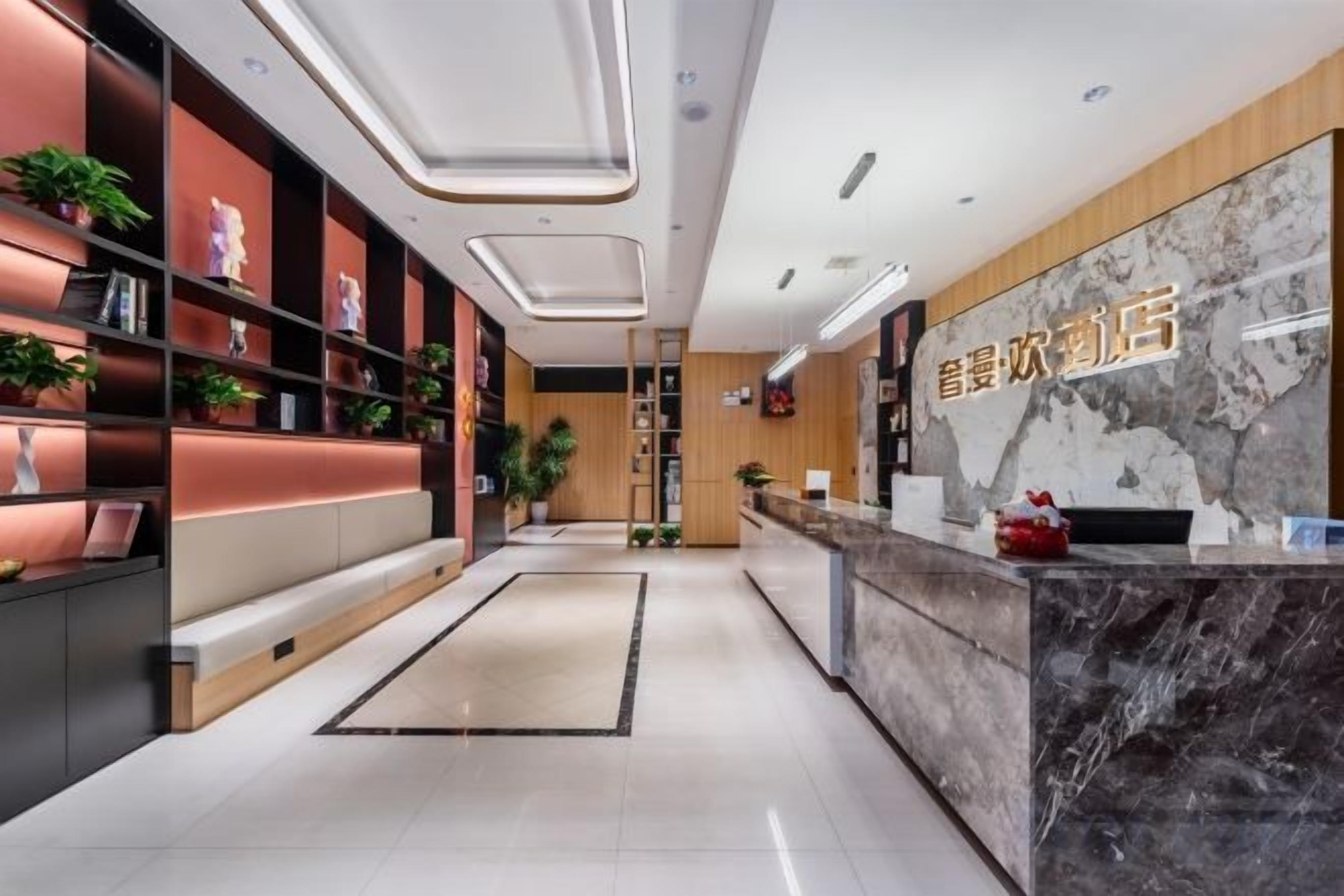 A hotel reception area with a marble counter, shelves with plants, and a seating area.