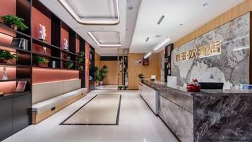 A hotel reception area with a marble counter, shelves with plants, and a seating area.