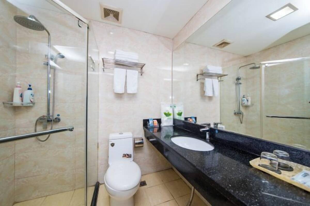 A modern bathroom with a glass shower enclosure, a white toilet, a black countertop with a sink and mirror, and a towel rack.