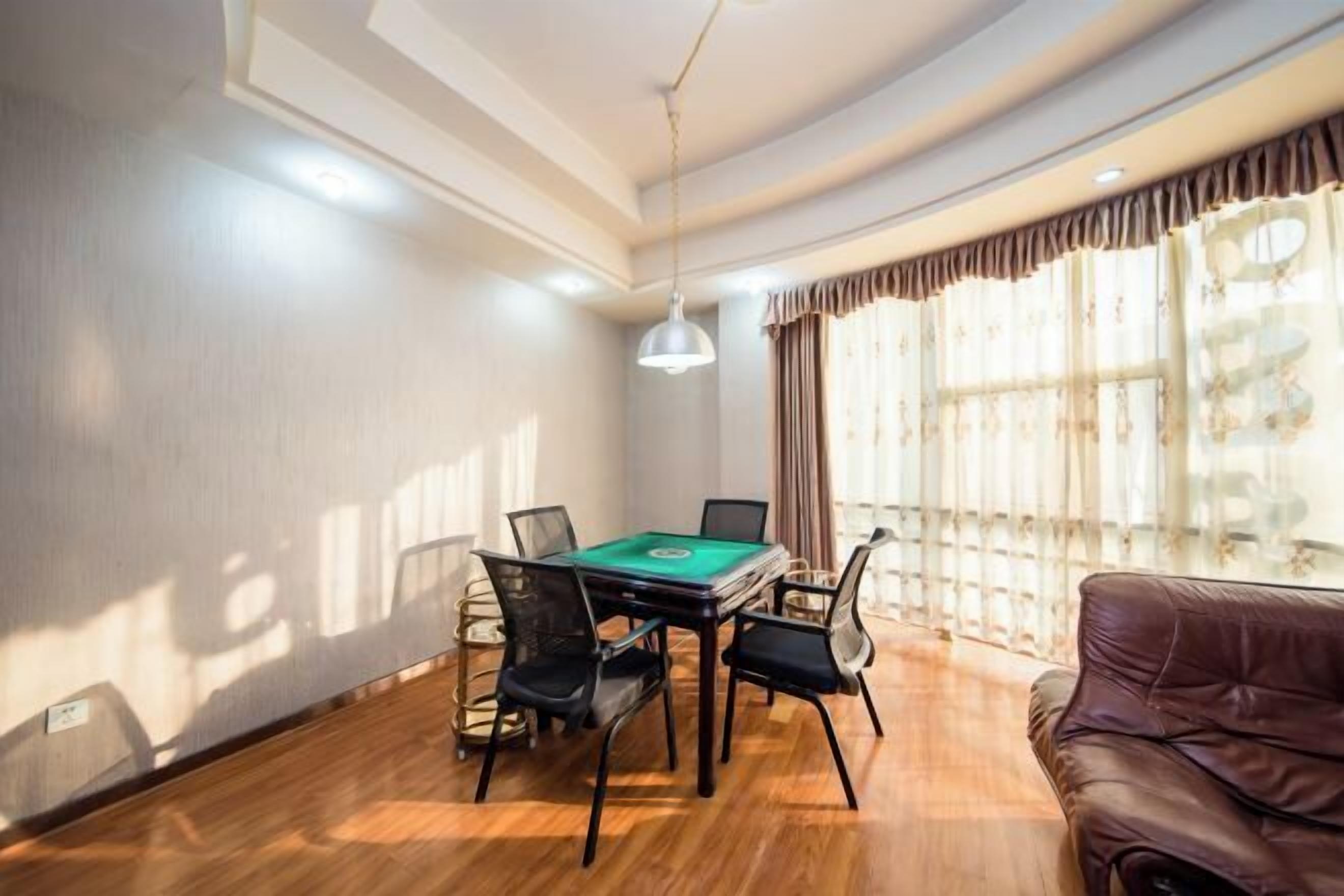Una habitación con mesa de billar, cuatro sillas, un sofá de cuero marrón y ventanas grandes con cortinas.