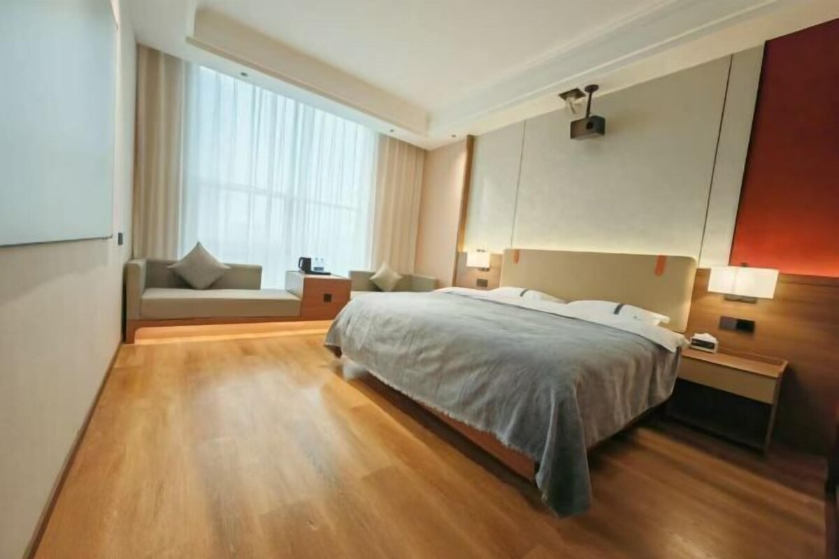 A hotel room with a large bed, a sofa, a nightstand, and a window with curtains.