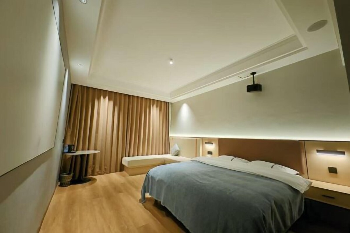 A modern bedroom with a bed, bedside tables, a small table, and a wall-mounted light fixture.
