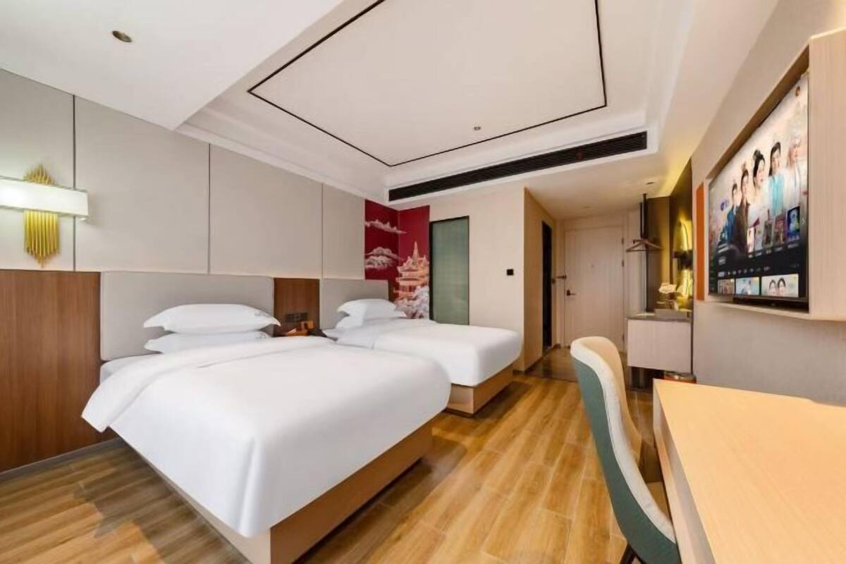 A hotel room with two beds, a desk, and a TV.
