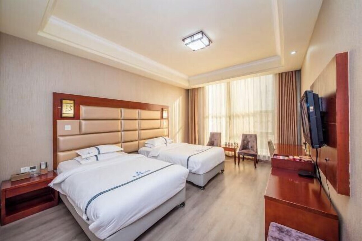 A hotel room with two beds, a TV, a desk, and a window with curtains.