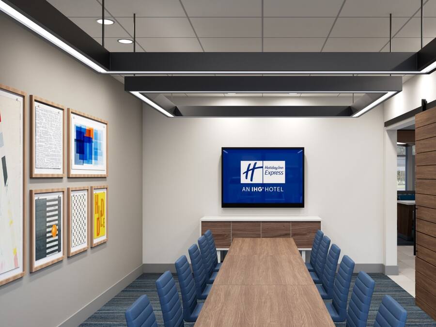 Ein Konferenzraum mit einem langen Tisch, blauen Stühlen, gerahmten Kunstwerken an den Wänden und einem großen Bildschirm, der das Holiday Inn Express Logo zeigt.