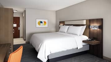 Ein modernes Hotelzimmer mit einem großen Bett, einem Schreibtisch und einem Sessel. Ein Nachttisch mit Telefon und Lampe steht bereit. Der Boden ist mit Teppich ausgelegt und an der Wand hängt ein Bild.