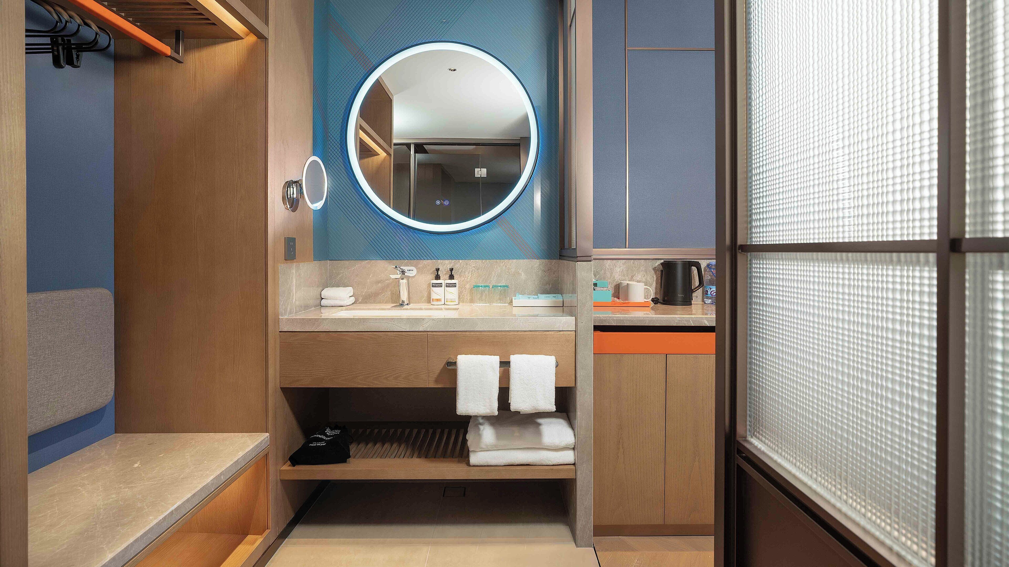 A modern bathroom with a round mirror, wooden vanity, and a shower area.