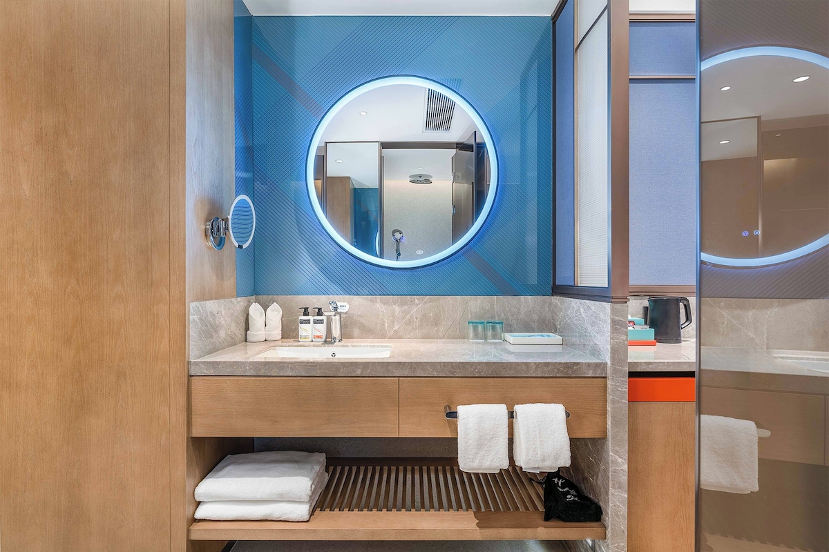 A modern bathroom with a wooden vanity, a round mirror, and a built-in sink.