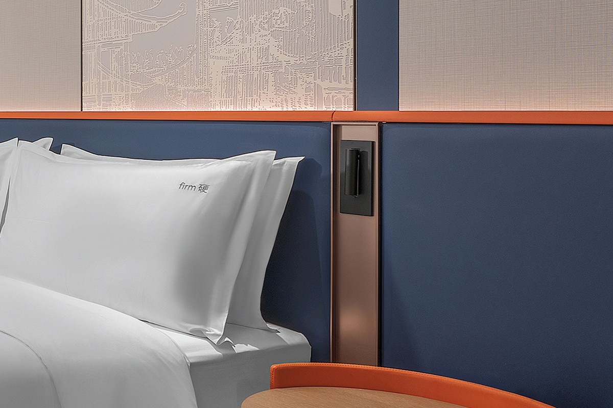 A hotel room with a bed, a nightstand, and a wall with a decorative panel.
