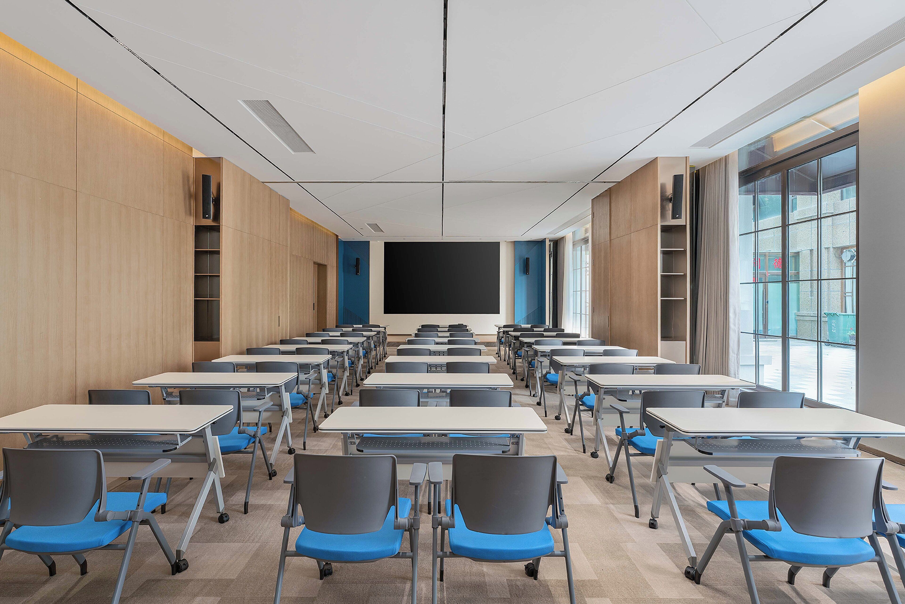 A classroom with rows of desks and chairs, a large blackboard, and a window providing natural light.