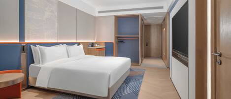 A modern hotel room with a large bed, a bedside table, a wardrobe, and a bathroom visible through an open door.