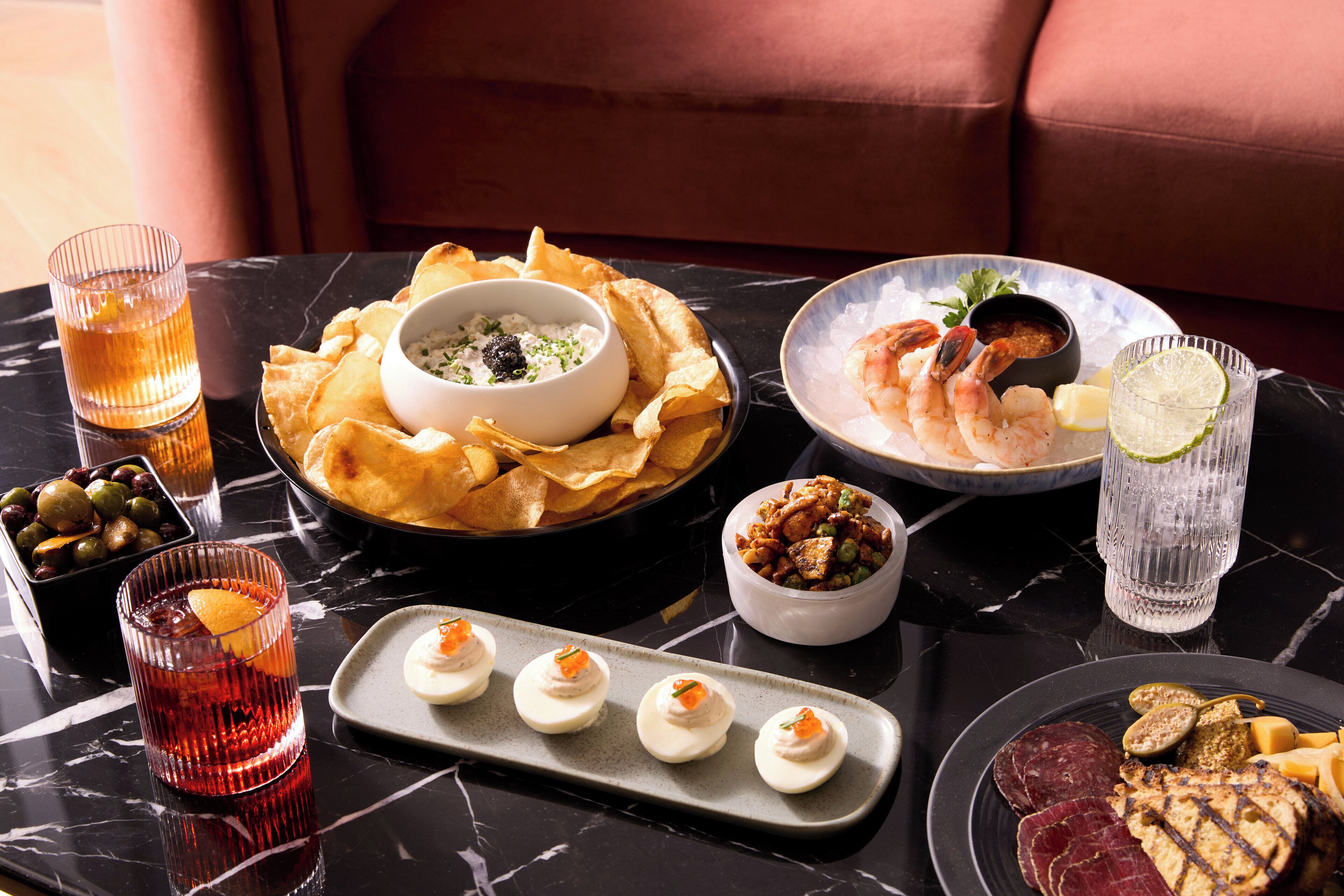 A dining table with various dishes, including shrimp, chips, and a bowl of dip. There are also glasses of a red beverage and a clear drink.