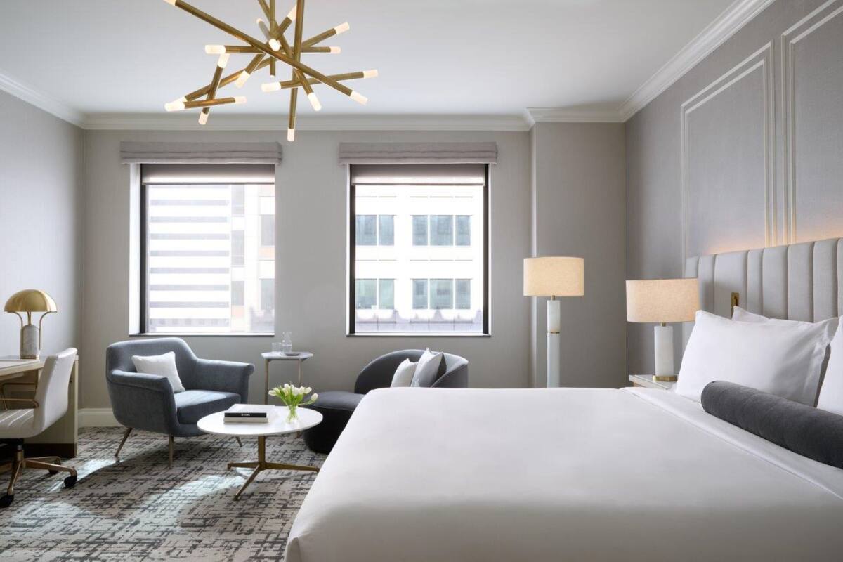 Habitación de hotel moderna con una cama grande, dos sillones, una mesita redonda y un candelabro.