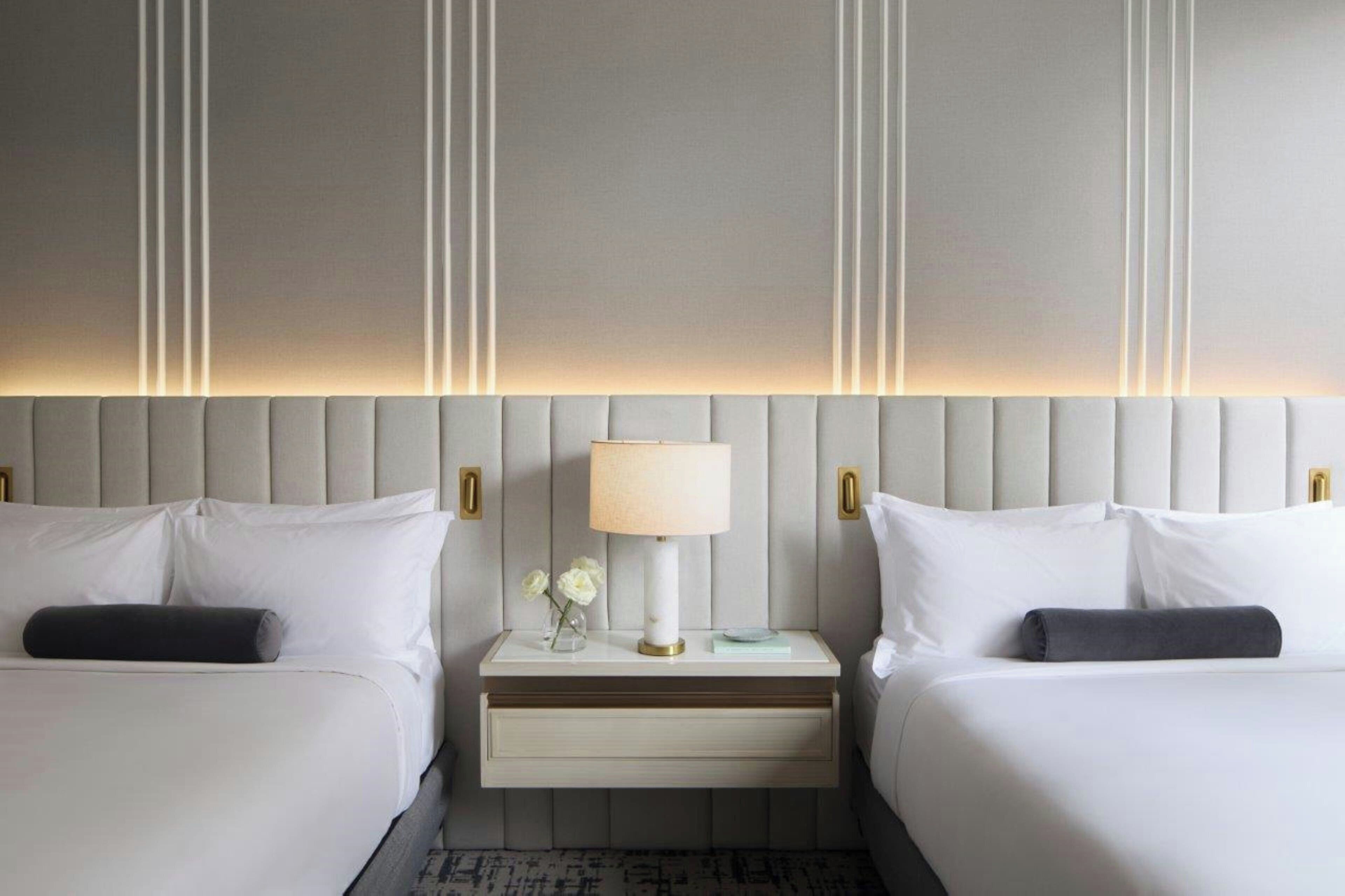 A hotel room with two beds, a nightstand with a lamp, and a decorative wall panel.