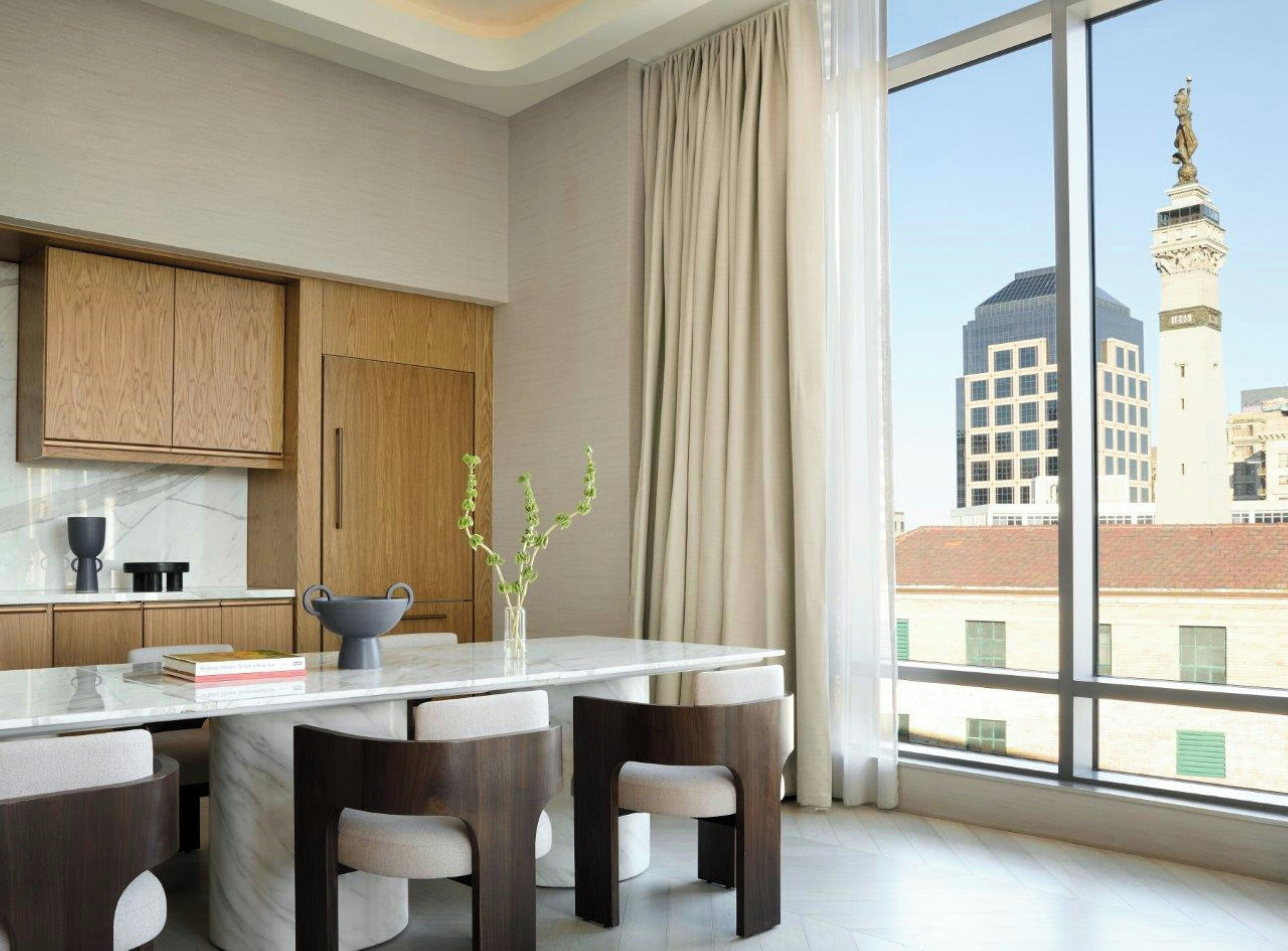 A modern kitchen with wooden cabinets, a marble countertop, and a view of a cityscape including a tower.