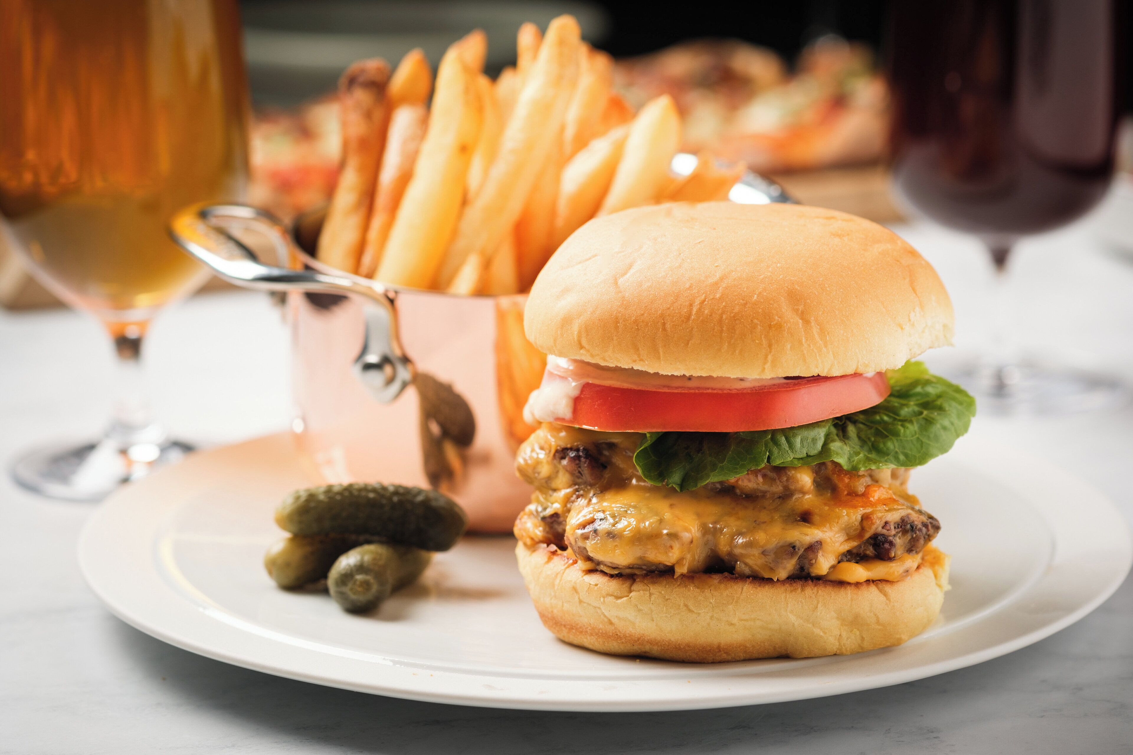 A burger with a bun, lettuce, tomato, and cheese, accompanied by fries and pickles on a plate.