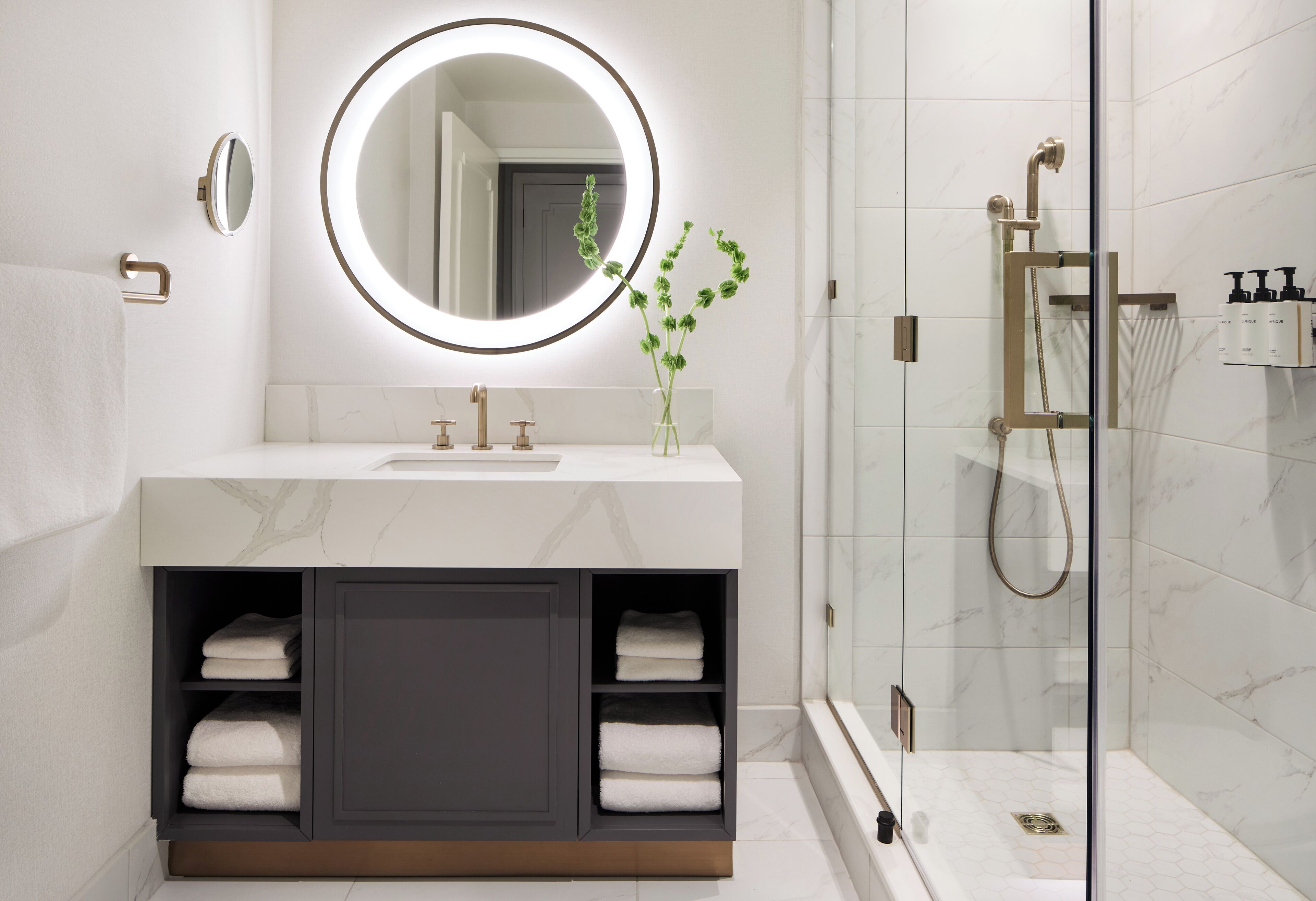 A modern bathroom with a marble vanity, a round mirror, and a glass-enclosed shower.