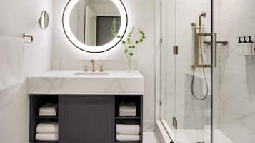 A modern bathroom with a marble vanity, a round mirror, and a glass-enclosed shower.