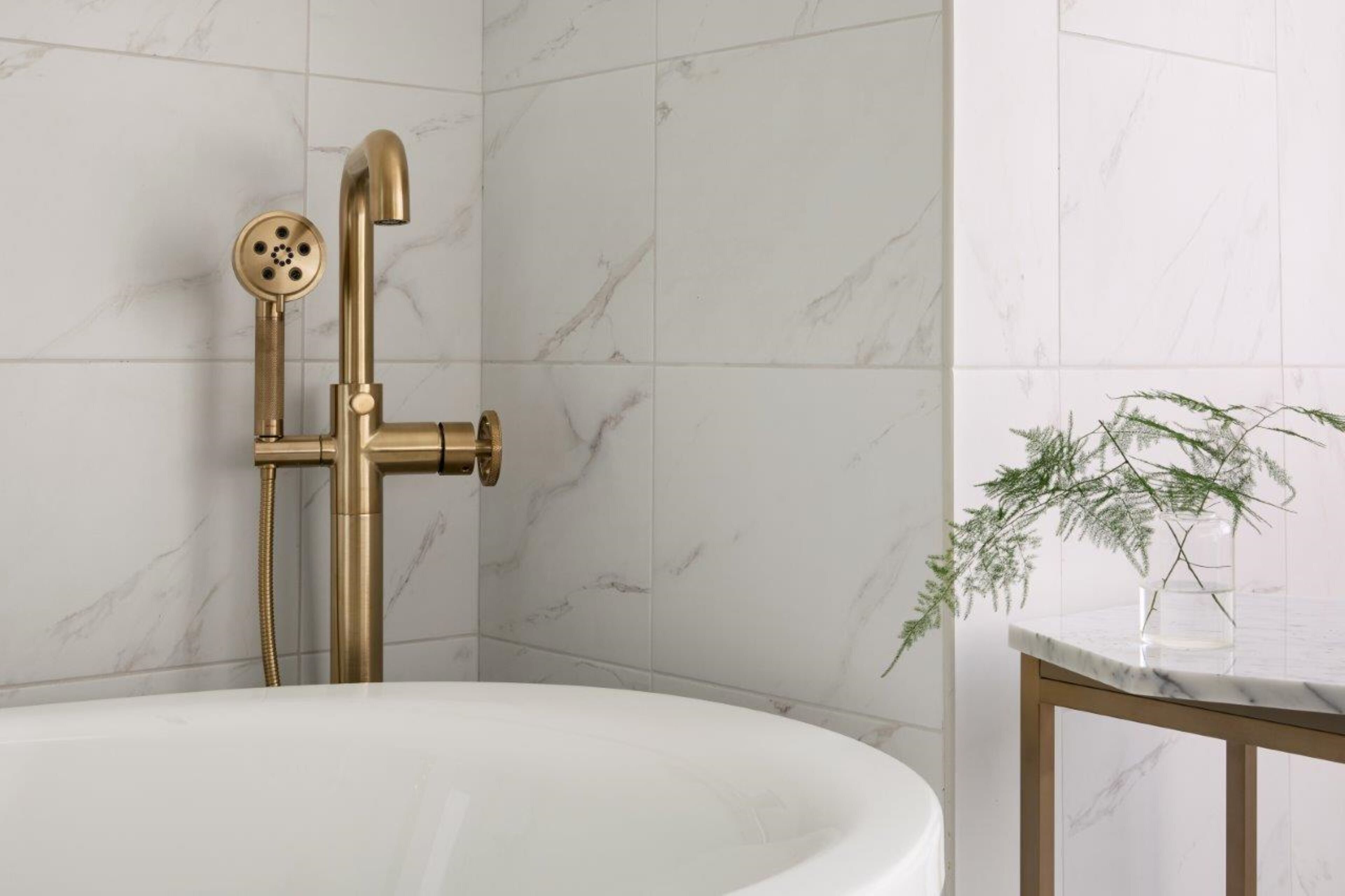 Une salle de bain avec une baignoire blanche, une pomme de douche dorée et un mur en marbre.