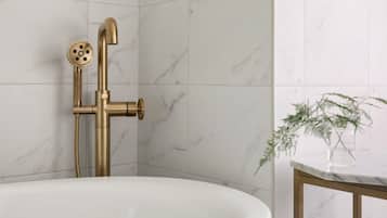 A bathroom with a white bathtub, a gold showerhead, and a marble wall.