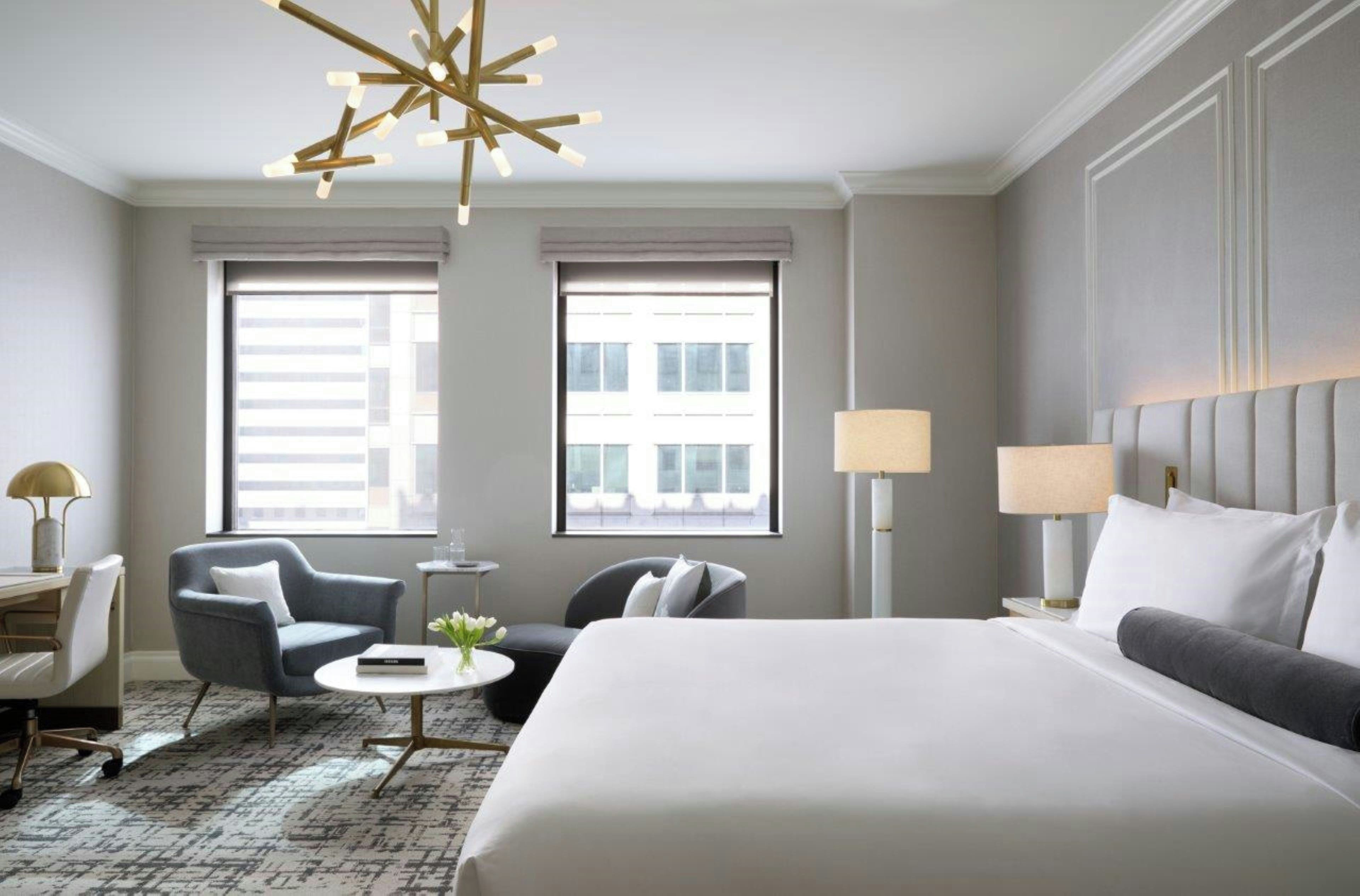 A hotel room with a large bed, two armchairs, a small round table, and two floor lamps.