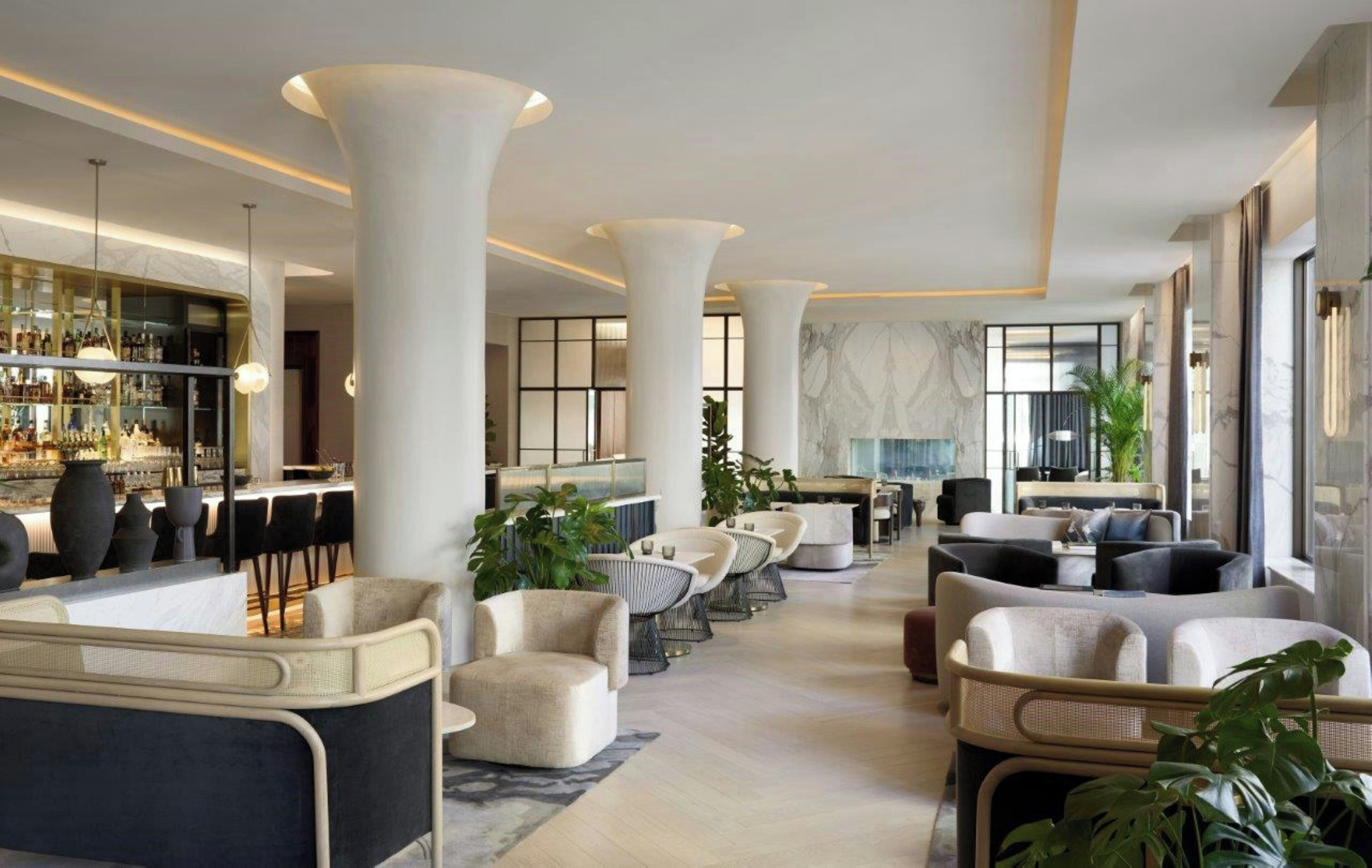 Un amplio vestíbulo de hotel con techos altos, grandes columnas, una zona de bar y cómodos asientos.