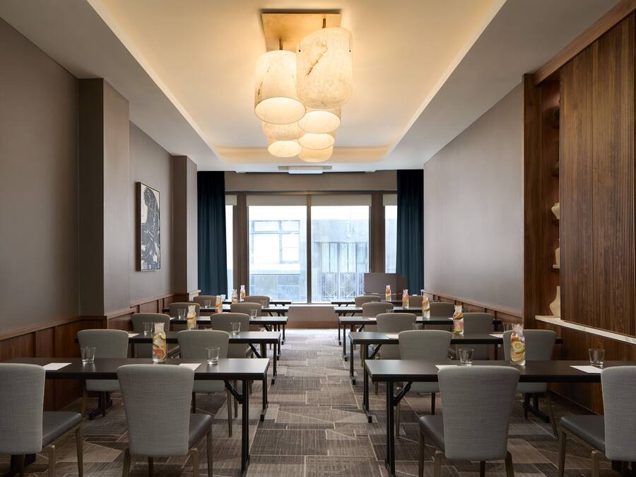 A conference room with tables and chairs, large windows, and a modern chandelier.