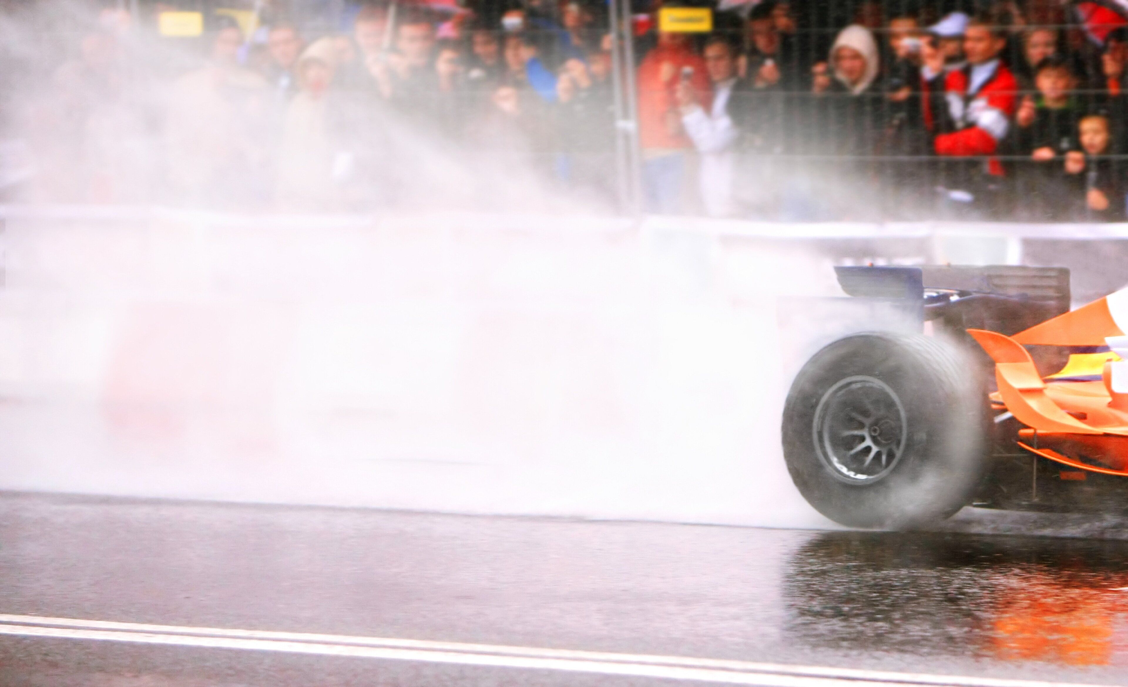 A racing car on a wet track with smoke, indicating a high-speed event.