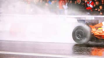 A racing car on a wet track with smoke, indicating a high-speed event.