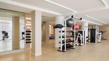 A modern gym with exercise equipment, a mirrored wall, and a wooden floor.