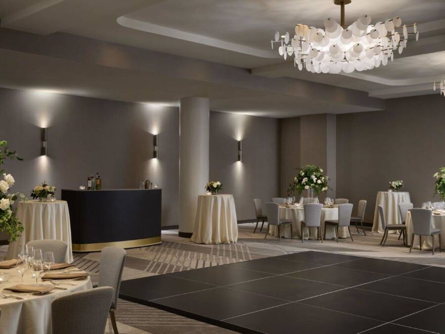 En moderne hotellobby med runde borde, en receptionsdisk og et stort, sort dansegulv.