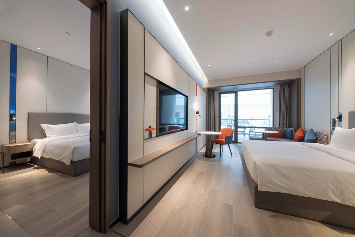 A modern hotel room with two beds, a TV, a desk, and a balcony with a view.