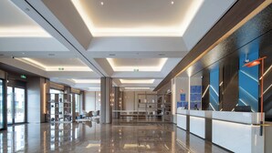 Un hall d’hôtel moderne comprenant un comptoir d’accueil, un espace salon et une grande fenêtre offrant une vue sur l’extérieur.