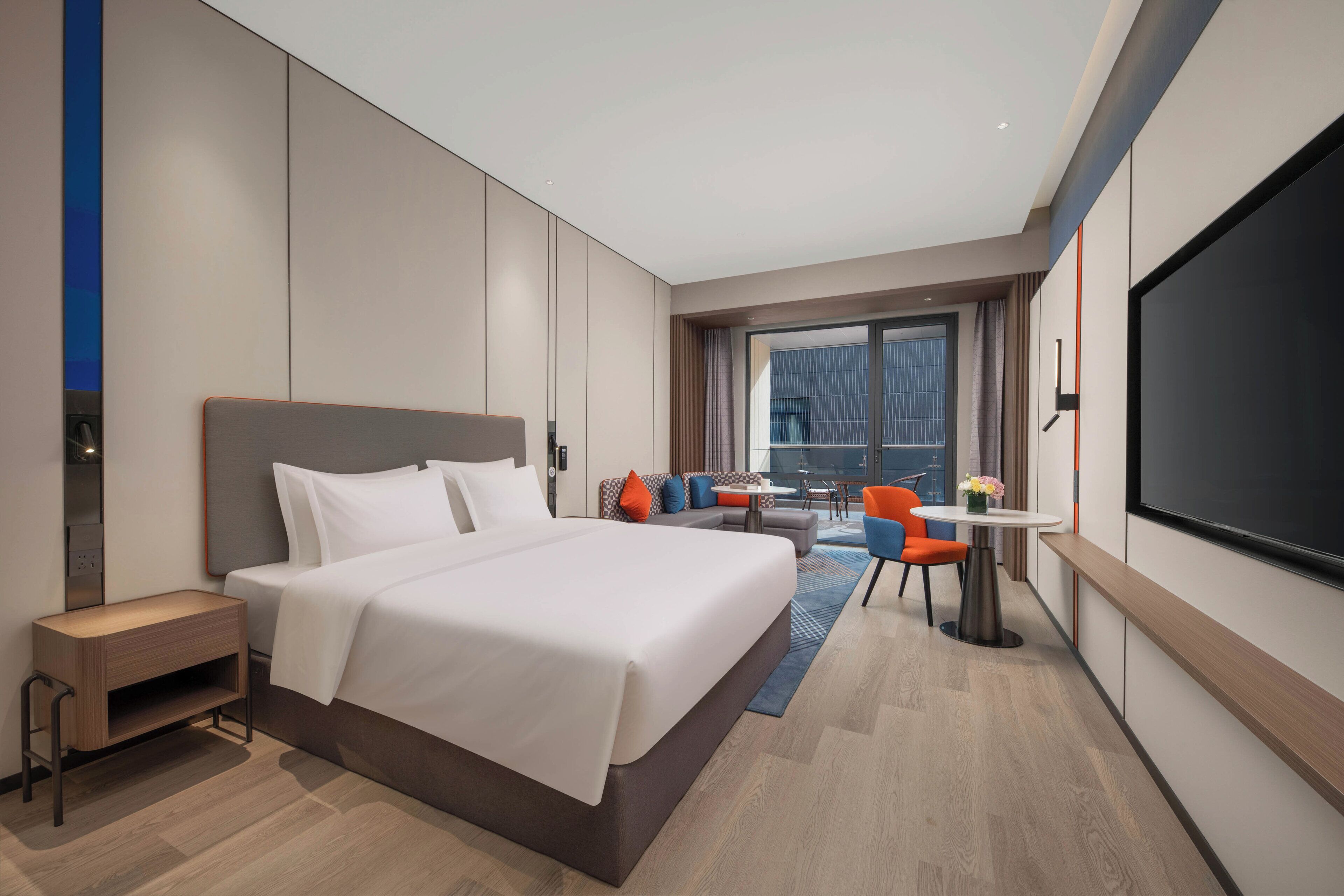 A modern hotel room with a large bed, a desk, a chair, and a TV.