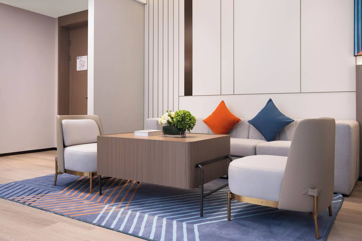 A modern hotel room with a sofa, armchairs, a coffee table, and a patterned rug.