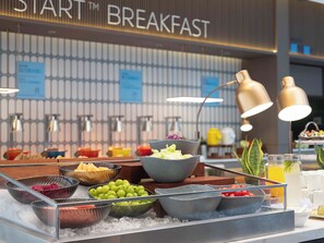 A breakfast buffet with various fruits and beverages, a sign reading "START BREAKFAST", and a modern interior design. - Holiday Inn Express Hai'an Railway Station by IHG (Nantong)