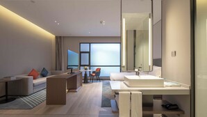 Une chambre d’hôtel moderne dotée d’un grand lit, d’un coin salon avec un canapé et des fauteuils, d’une table à manger et d’un grand miroir.