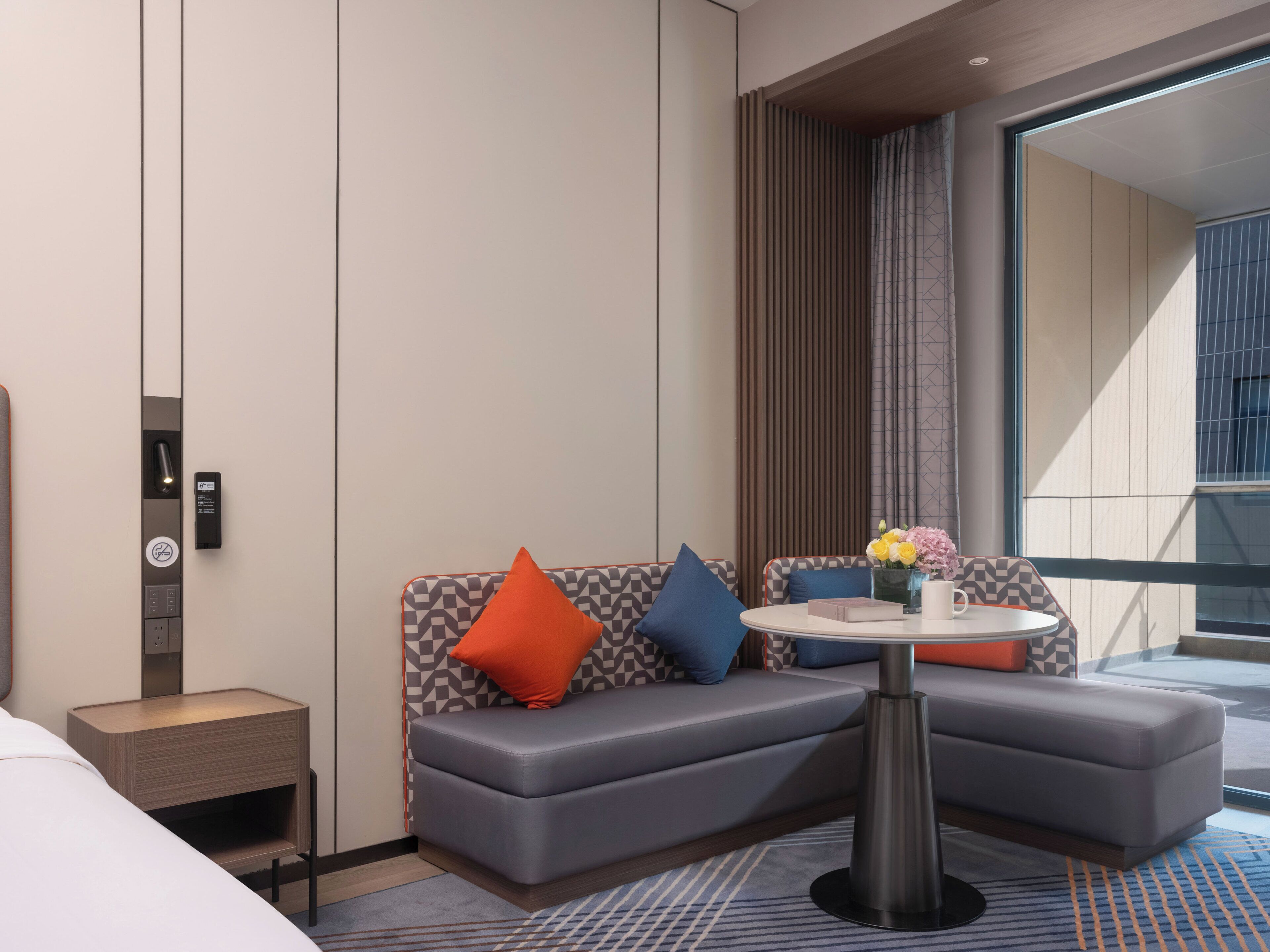 Una habitación de hotel moderna con un sofá, una mesita, una mesita de noche y un ventanal grande.