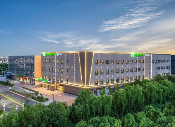 A Holiday Inn Express hotel with a modern design, featuring a large parking area and a well-maintained garden. - Holiday Inn Express Hai'an Railway Station by IHG (Nantong)