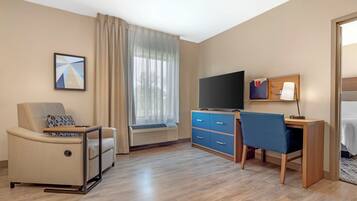 A hotel room with a sofa, a desk, a television, and a bed.