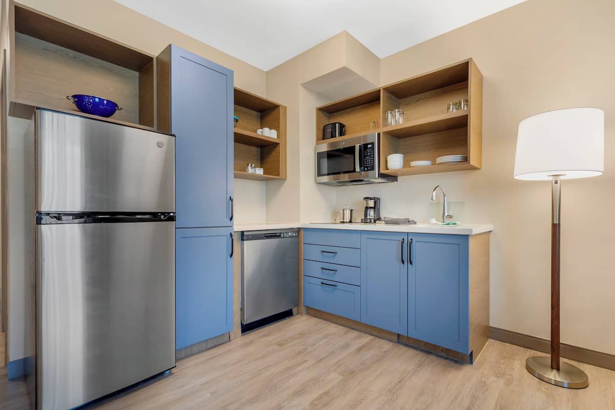 A modern kitchen with blue cabinets, stainless steel appliances, and wooden shelves.
