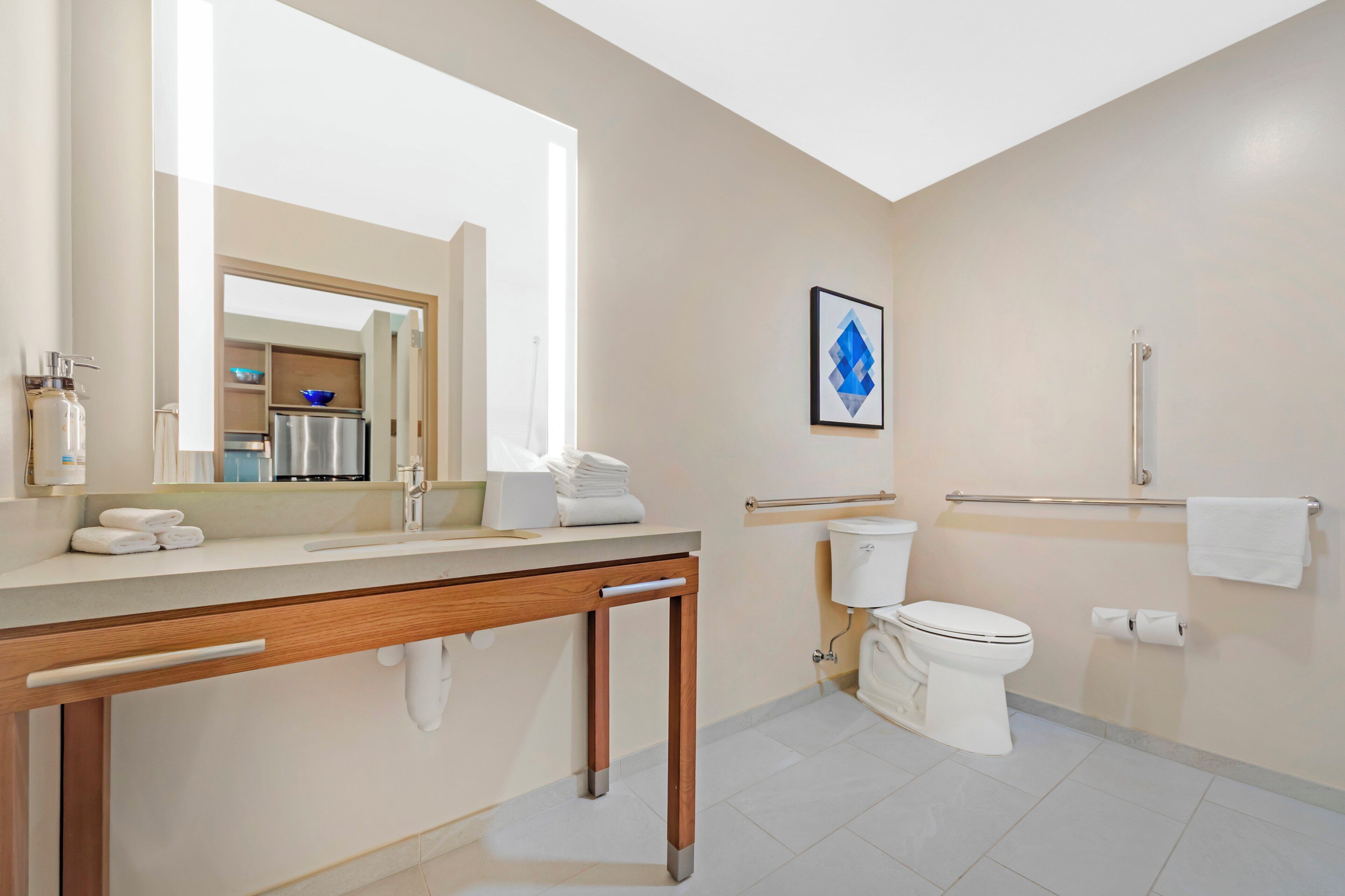 Een moderne badkamer met een houten wastafelmeubel, een grote spiegel, een toilet en een kunstwerk in een lijst aan de muur.