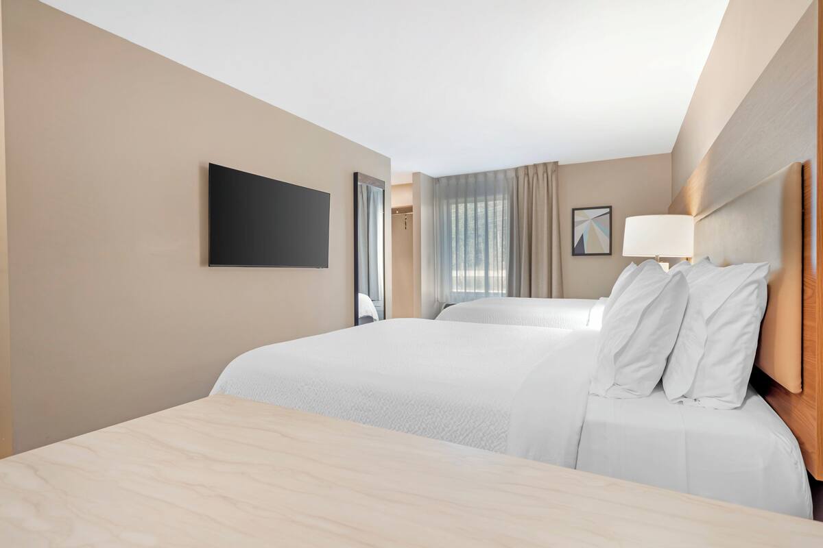 A hotel room with two beds, a flat-screen TV, a bedside lamp, and a window with curtains.