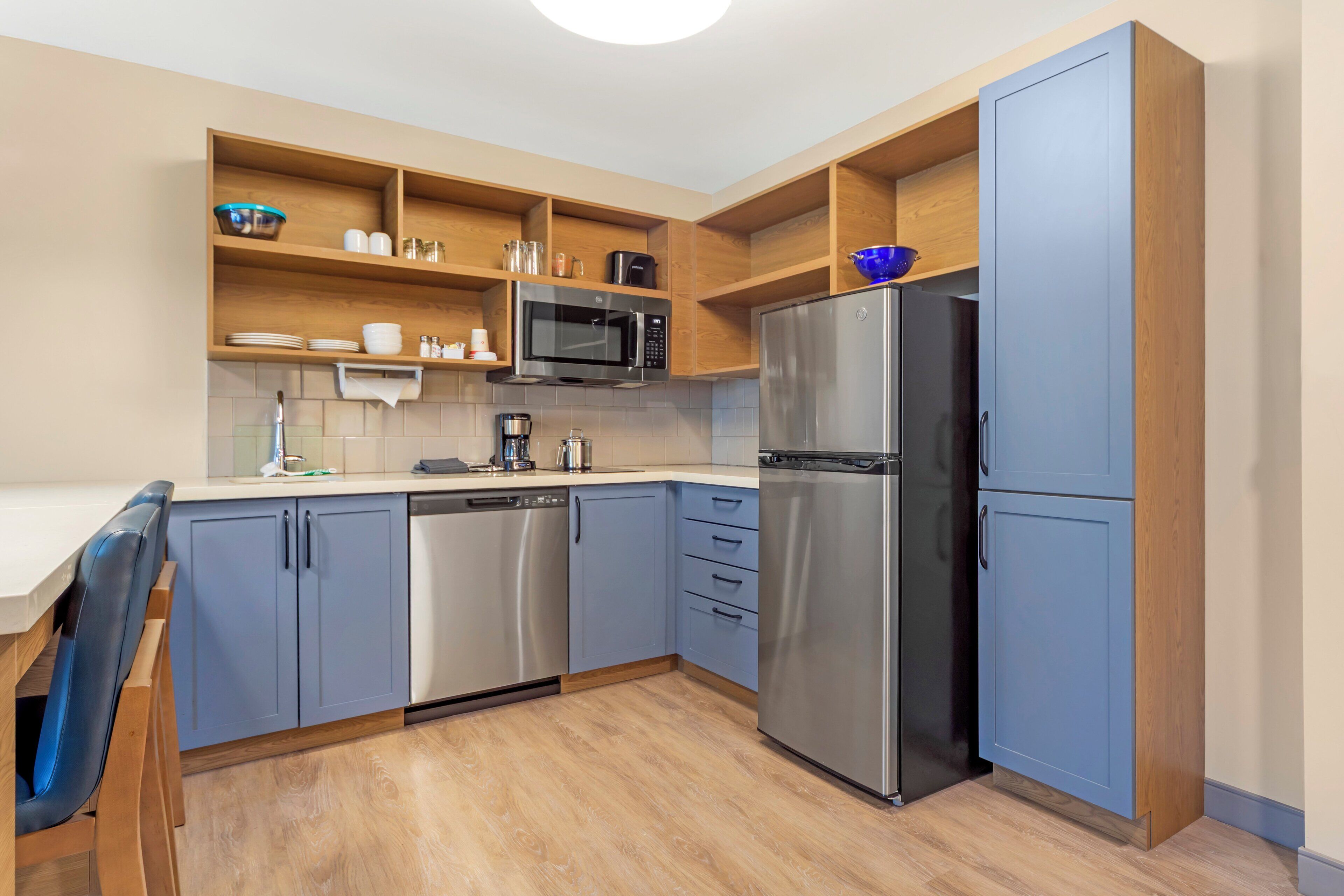 A modern kitchen with blue cabinets, a stainless steel refrigerator, a microwave, and a dishwasher.