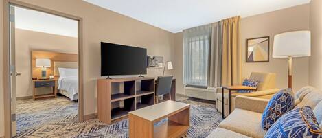 Una habitación de hotel con sofá, televisor, escritorio, silla y cama.