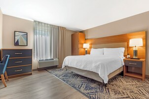 Habitación de hotel con cama, mesitas de noche con lámparas, escritorio con silla, ventana con cortinas y aire acondicionado de pared.