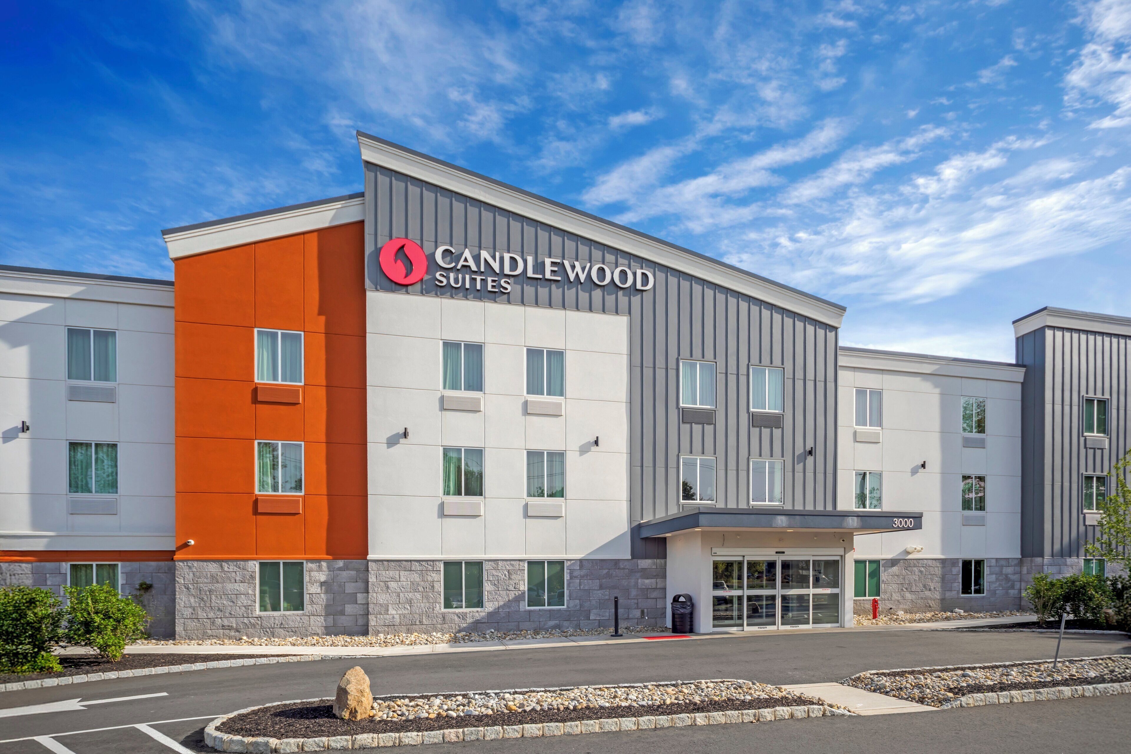 Un hotel modern amb un cartell prominent de "Candlewood Suites", façana de pedra i un pàrquing.