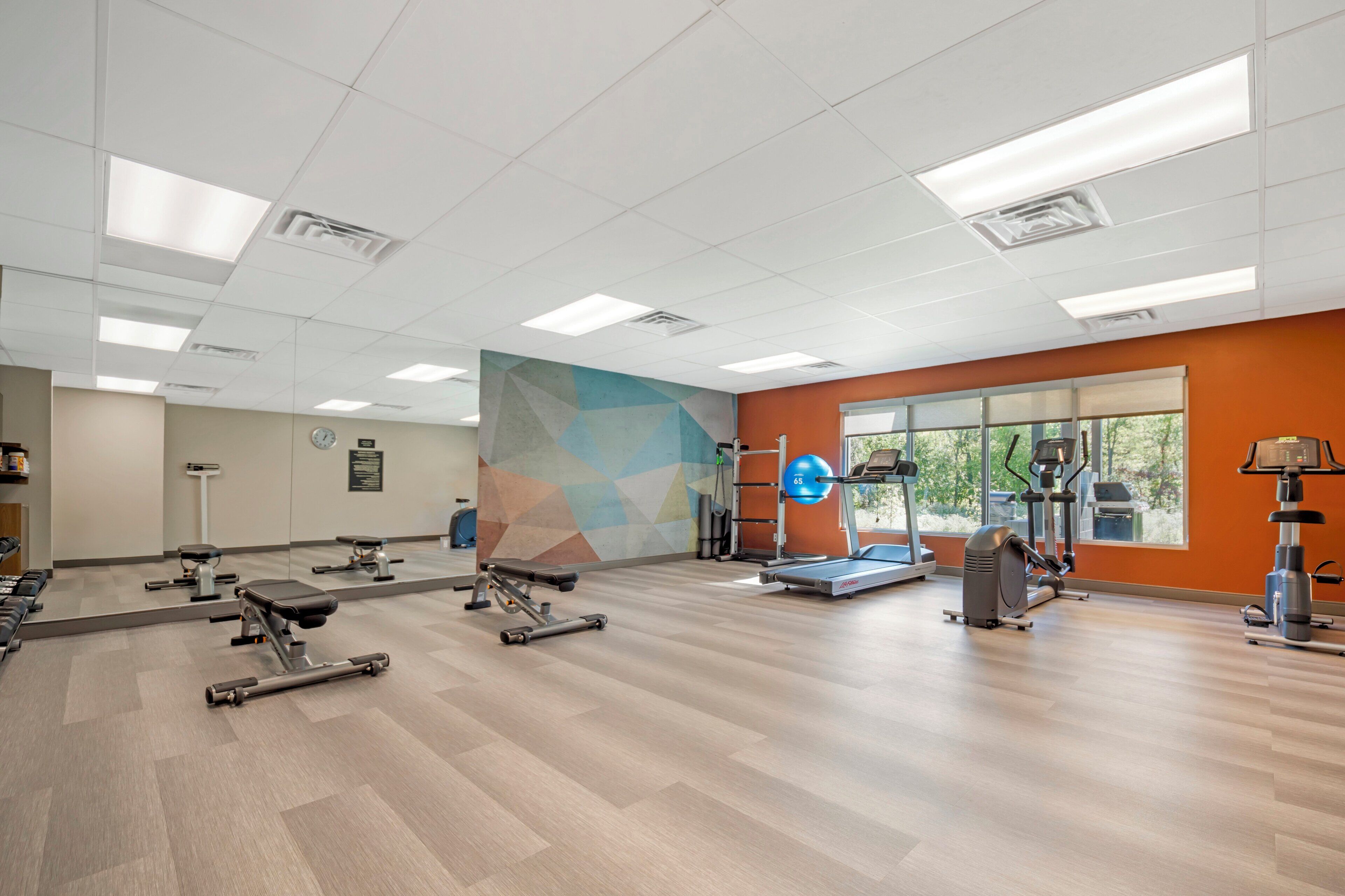Un gimnasio moderno con diversos equipos de ejercicio, amplias ventanas y un diseño de pared geométrico.